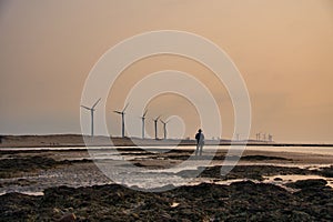 Silhouette of a man  standing on a lake shore during sunset, with the wind turbines