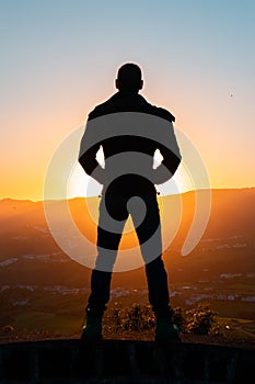 Silhouette of man standing a lone on top of mountain with orange twilight in the dark evening light from the back