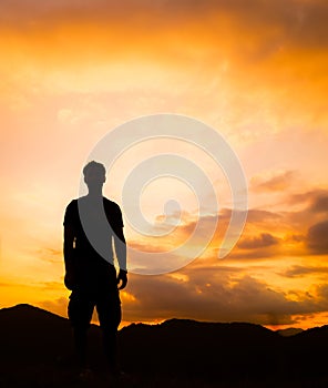 Silhouette of man standing a lone on top of mountain with orange twilight