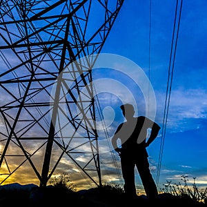 Silhouette of man standing beside a power tower