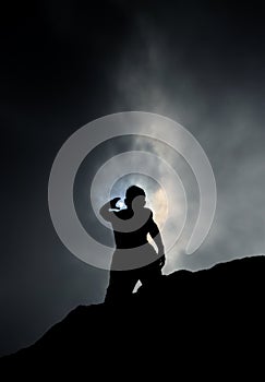 Silhouette of Man Standing on Rock Reaching up to the Sky during Partial Eclipse