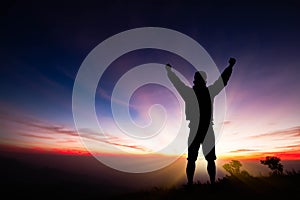 Silhouette of man standing on top of mountain with fists raised up, successful, achievement and winning concept