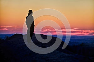 Silhouette of a man standing on top of a mountain and looking at the sunset