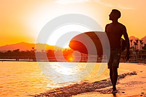 Silhouette man surfer in sunset light walking down beach with surfboard near waters edge enjoying summer time practice