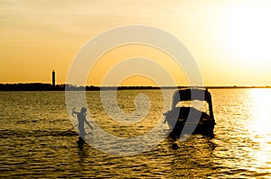 Silhouette of a man taking anchor for a boat with setting sun in the distance