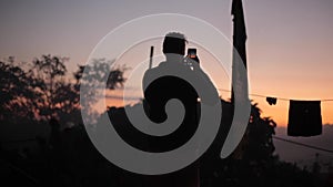 A silhouette of a man taking pictures of sunset, sunrise. Village, laundry drying on a line outdoors.