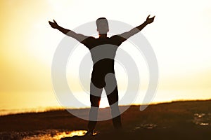 Silhouette of man with their hands raised in the sunset at the sea.