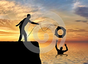 A silhouette of a man throws a lifeline to another man who is drowning in the water