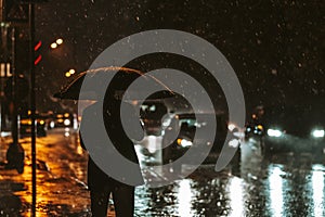 Silueta z muž deštník v podsvícení z světlomety v noci během. těžký déšť v město 