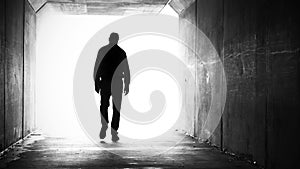 A silhouette of a man walking out of a dark tunnel towards the light