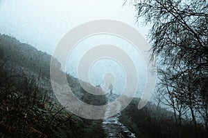 A silhouette of a man walking on path in the countryside, on a spooky foggy winters day. With a grunge, vintage muted edit