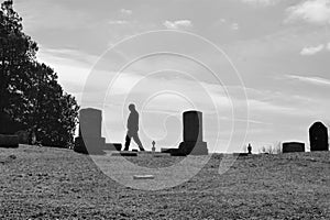 Silhouette of man walks among headstones on hill in cemetery