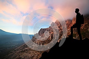 Silhouette of a man who stands on top of the mountain, against the backdrop of sunset mountains.