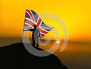 Silhouette man winner waving british flag on top of the mountain