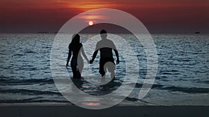 Silhouette of the man and woman, going to the sea on a sunset and kissing in waves