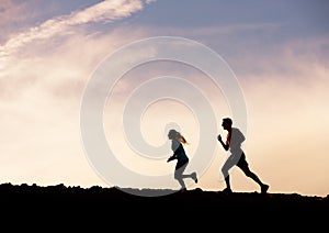 Silhouette of man and woman running jogging together into sunset