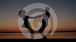 Silhouette Of Man And Woman At Sunset By The Beach Holding Hands And Circling
