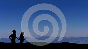 Silhouette man and woman trail runner with sky at sunrise while running in the mountains.