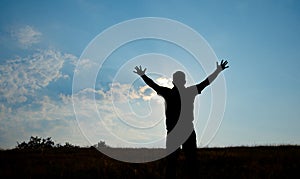 Silhouette of man worship with hands raised to the sky in nature