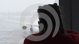 Silhouette of a Masked Young Woman at Airport Terminal Window Looking at Planes