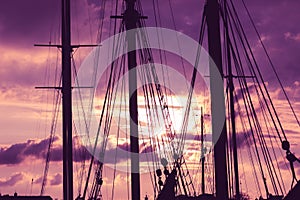 Silhouette of masts and ropes of a wooden old sailing ship against the background of the evening dark pink purple neon magical sky