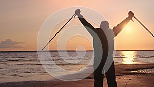 Silhouette mature man raising up Scandinavian walking stick sunset sun sea beach healthy lifestyle