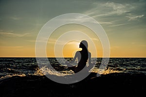 Silhouette meditation girl lotus position on stone on the background of the stunning sea.