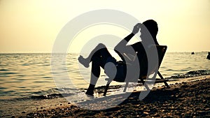 Silhouette men in chair reading book on the beach sunset