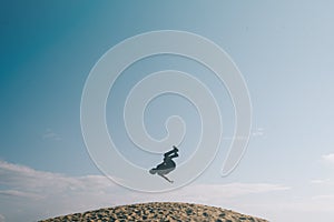 Silhouette of a men doing an acrobatic backflip move on sand dunes.