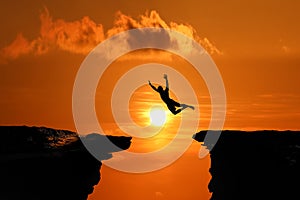 Silhouette of Men are jumped between high cliff at a red sky sunset