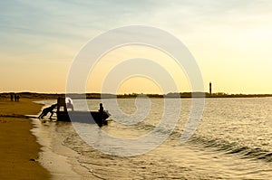 Silhouette of men pushing a tourist fishing boat into the ocean at a Gujarat beach