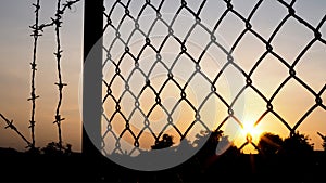 Silhouette of mesh fence and barbed wire with dark sky at sunset