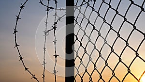 Silhouette of mesh fence and barbed wire with dark sky at sunset