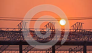 Silhouette of metal roof outline of industrial building structure with cable lines in construction site at sunset