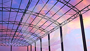 Silhouette of metal roof structure of industrial building against sunset sky background