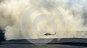 Silhouette of military helicopter landing or taking off in a dust cloud
