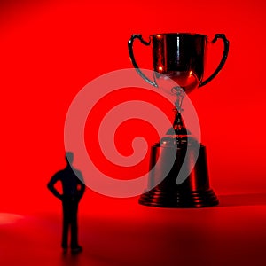 Silhouette of miniature man and a trophy. Sport success concept. Red background, shallow depth of field