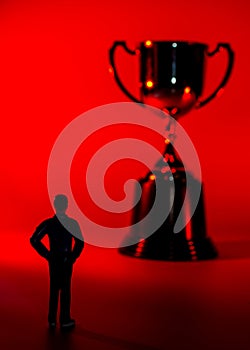 Silhouette of miniature man and a trophy. Sport success concept. Red background, shallow depth of field