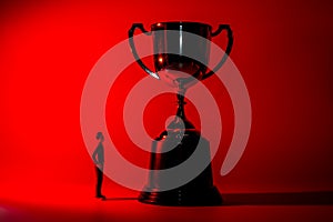 Silhouette of miniature man and a trophy. Sport success concept. Red background, shallow depth of field