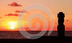 Silhouette of Moai wearing hat called Pukao at Ahu Ko Te Riku ceremonial platform against stunning sunset sky, Pacific ocean