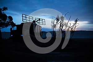 Silhouette of mobile air defence truck with radar antenna during sunset. Satellite dishes or radio antennas against evening sky