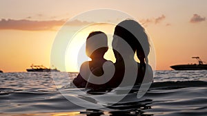 Silhouette Of Mom And Baby Swimming In Seawater At Resort Against Shines Sunset