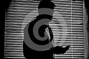Silhouette in monochrome of man with his mobile phone iPhone in darkness