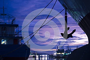 Silhouette mooring rope with anchor of cargo ships docked at port on riverside against twilight sky background