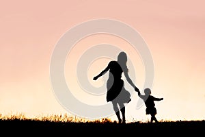 Silhouette of Mother and Baby Daughter Running and Dancing at Sunset