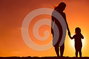 Silhouette of mother and daughter holding hands at sunset