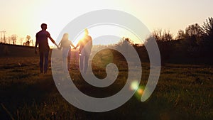 Silhouette of mother and father walking with their daughter at sunset