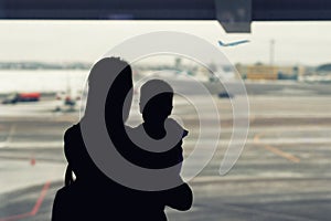Silhouette of mother holding on hands little toddler boy with window of airport on background. Departure and arrival. Single