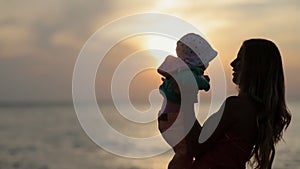 Silhouette of mother holding toddler on hands at