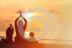 Silhouette of mother and kids doing yoga at sunset